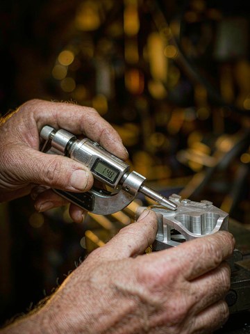 An engineer measuring a machined aluminum prototype with a digital micrometer