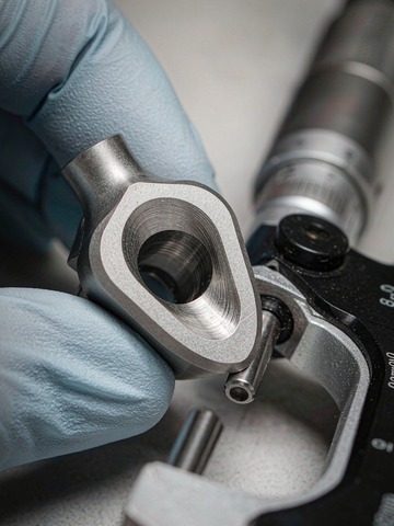 Machinist in clean gloves inspecting a titanium medical part with a digital micrometer on a controlled inspection bench