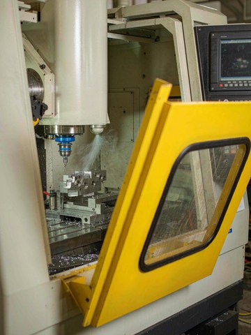 Three-axis CNC mill machining an aluminum prototype bracket with chip evacuation