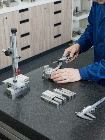 Inspector measuring a machined aluminum part with a digital micrometer on a granite surface plate