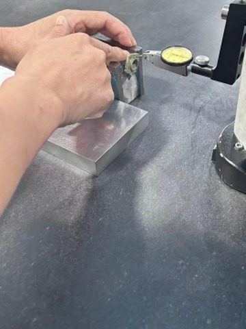 A lever type dial indicator set against a machined part on a surface plate during a bench inspection check