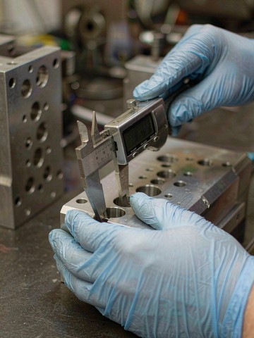 Digital caliper checking hole spacing on an aluminum plate, a size-only check where plus/minus tolerances are enough