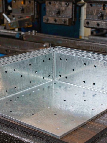 Freshly folded sheet metal brackets with a CNC press brake in the background