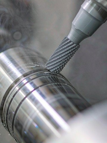 A spiral cam groove milled into an aluminum optical lens barrel on a five-axis center.