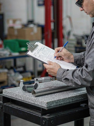 Quality inspector recording dimension results with a digital micrometer beside a first article inspection report.