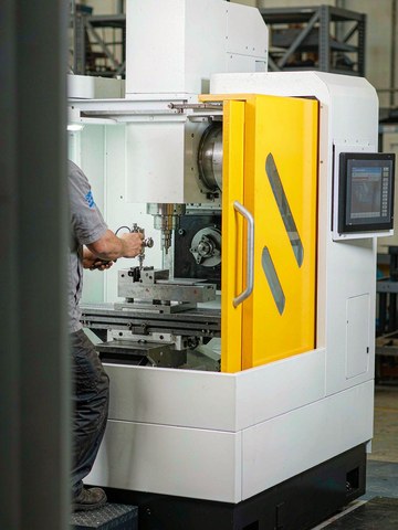 Machinist indicating a vise fixture on a compact vertical machining center with white enclosure and yellow doors before a production run.