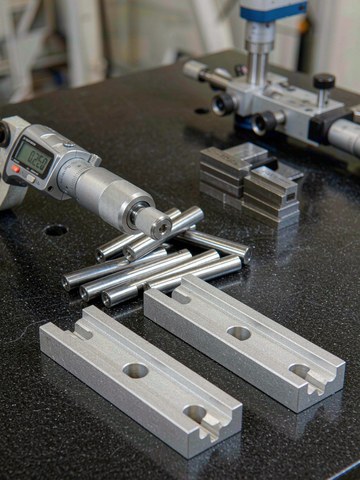 Precision aluminum and steel parts checked with a digital outside micrometer on a granite surface plate.